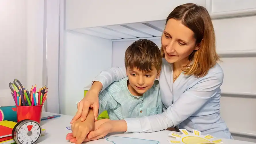 Mother patiently teaching her autistic son at a desk, raising awareness about aluminum and autism.